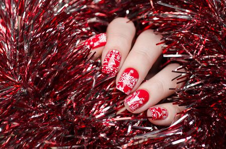 red Christmas manicure with deer and snowflakes and Norwegian pattern on the background of shiny tinselの写真素材