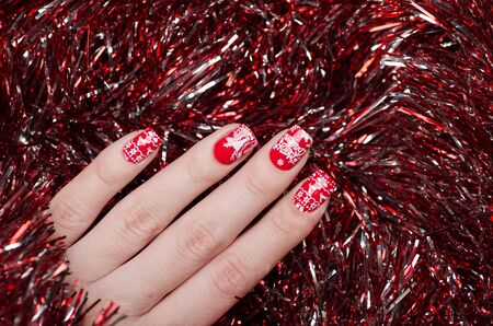 red Christmas manicure with deer and snowflakes and Norwegian pattern on the background of shiny...