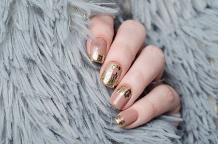 beige manicure with gold lace pattern on gray backgroundの写真素材