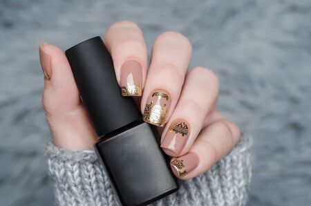 beige manicure with gold lace pattern on gray background