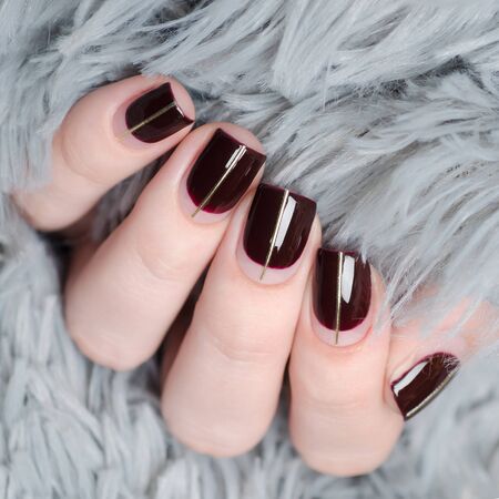 Burgundy manicure with negative space and Golden line on grey fur backgroundの写真素材