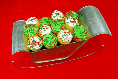 Festive cupcakes displayed in Santa s sleigh  The sleigh sits on a poinsettia-decorated tablecloth の写真素材