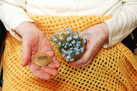 Elderly woman holds forget-me-not flowers and the word Hope, engraved on a stone  Image created to support organizations and people who seek solutions for memory loss の写真素材