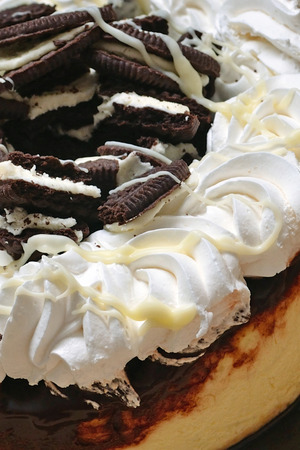Close-up of a cookies and cream chocolate marble cheesecake. This gourmet dessert has abundant cookie crumbles, whipped cream frosting, and melted white chocolate drizzled on top.の写真素材
