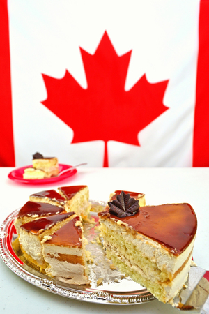 A slice of Maple Mousse Cake for Canada Day celebrations on July 1st. The focus is on the chocolate maple leaf. The Canadian Flag is blurred in the background providing copy space.の写真素材