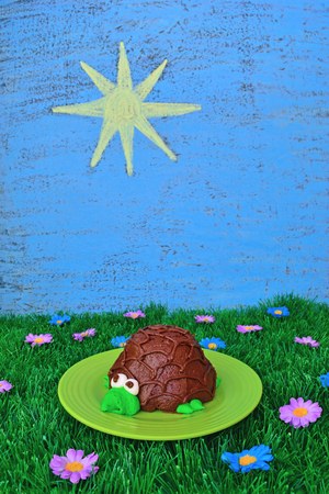 Summer food theme includes a turtle cupcake, artificial grass and flowers, plus the sky and sun drawn on a chalkboard.の写真素材