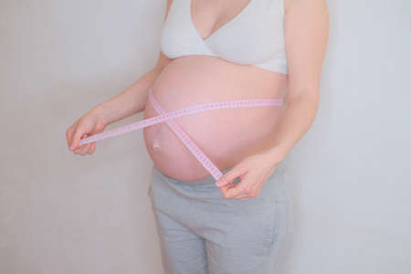 A pregnant woman is measuring her belly. Overweight concept.