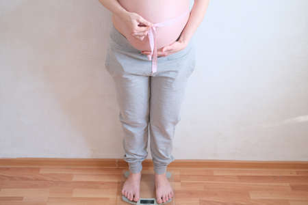 A pregnant woman is measuring her belly. Overweight concept.
