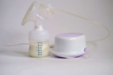 The electric breast pump is on the table in the kitchen. Breast pump with milk. Give expressed...