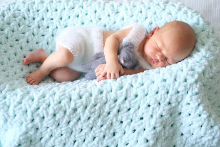 A sleeping newborn baby lies on a blue blanket, a crocheted toy mouse in the babys handsの写真素材