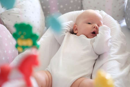 A newborn baby in white clothes lies in the crib and looks at his toys. Baby close upの写真素材