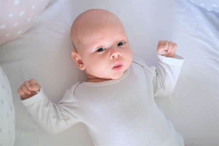 A newborn baby in white clothes lies on the bed. Portrait of a lying cute little child