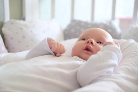 A newborn baby in white clothes lies on the bed. Portrait of a lying cute little childの写真素材