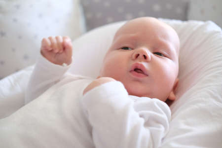 A newborn baby in white clothes lies on the bed. Portrait of a lying cute little childの写真素材