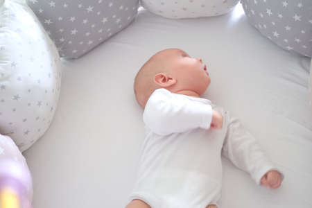 A newborn baby in white clothes lies on the bed. Portrait of a lying cute little childの写真素材