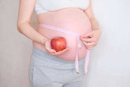 A pregnant woman holds a red apple in her hand. The concept of proper nutritionの写真素材