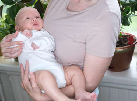 A beautiful young mother holds her newborn son in her arms by the window. Close-up portrait of a childの写真素材