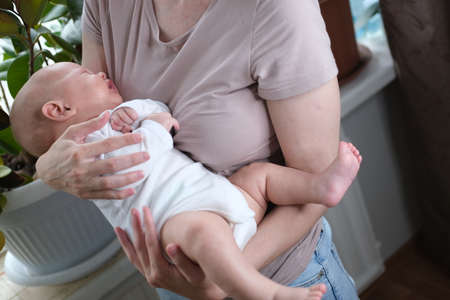 A beautiful young mother holds her newborn son in her arms by the window. Close-up portrait of a childの写真素材