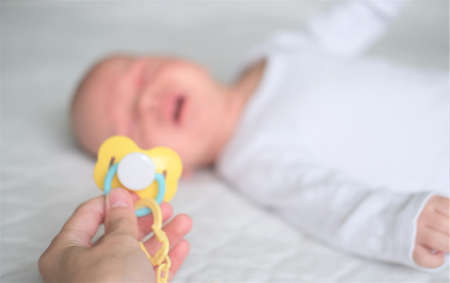 A newborn baby lies on a white blanket. The newborn baby is crying and does not want to take the...