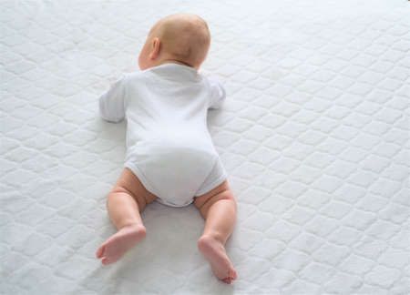 A newborn baby lies on a white blanket. The child learns to crawl.