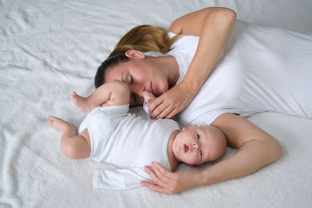 Beautiful young mother lies with her newborn baby on the bed.Portrait of mom and son in white clothes.の写真素材