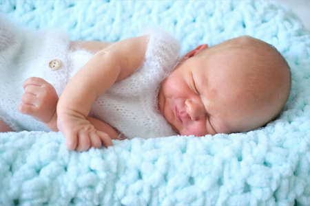 A sleeping newborn boy or girl lies on a blue wool blanket.Close-up portrait of a childの写真素材
