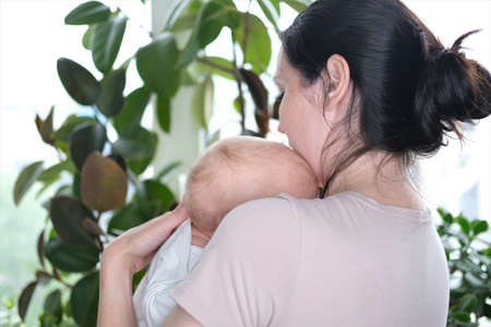 A beautiful young mother holds her newborn son in her arms by the window. Close-up portrait of a childの写真素材