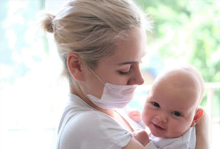 A young woman in a protective mask holds a newborn baby by the window.Portrait of a beautiful young woman and child.の写真素材