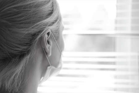 A young woman in a medical mask stands by the window.Prevention COVID-19の写真素材