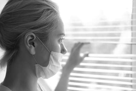 A young woman in a medical mask stands by the window.Prevention COVID-19.の写真素材