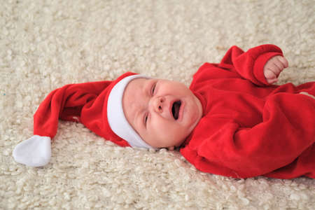 Baby in red costume and hat. Beautiful little baby celebrates Christmas.