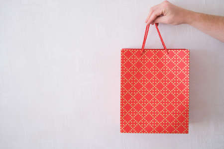 Male hand holds a red gift bag on a white background. A man gives a gift for a holiday.の写真素材
