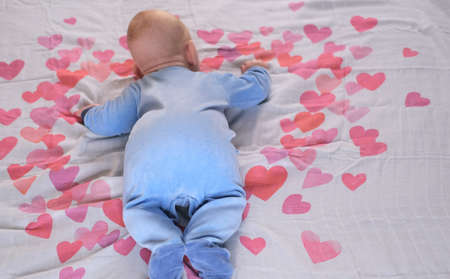Newborn baby - boy or girl lies on a white background with red and bright pink heartsの写真素材