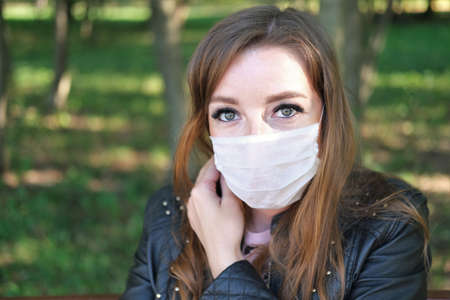 Girl in medical mask is resting on a bench in a park. Concept coronavirus, air pollution, restの写真素材