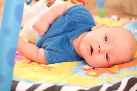 Newborn baby boy or girl playing. Portrait of a cute 3 month old baby lying on a bright blanket.の写真素材