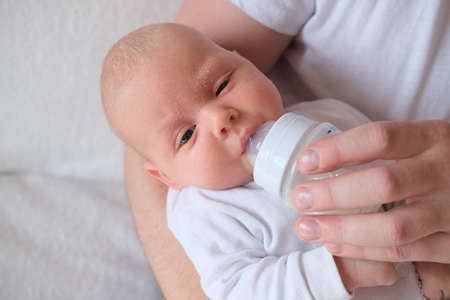 A father holds and bottle feeds his newborn baby. The baby has seborrhea on his face and head.の写真素材