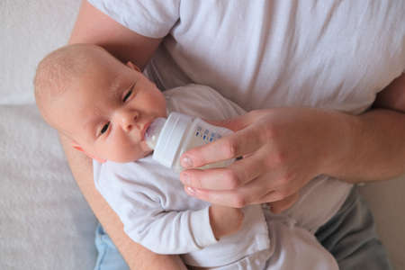 A father holds and bottle feeds his newborn baby. The baby has seborrhea on his face and head.