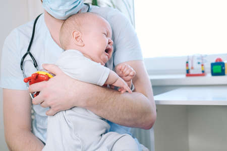 The pediatrician is holding a small child. The children's doctor listens to the boy with a stethoscopeの写真素材