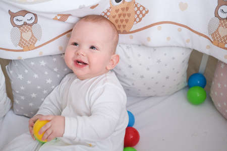 The kid plays with colorful balls in the crib.