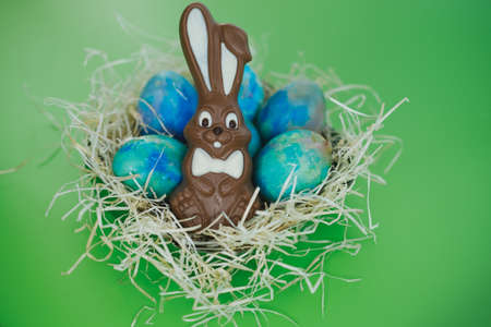 Chocolate Easter bunny lies in a basket with colorful eggs on a green background, close-up