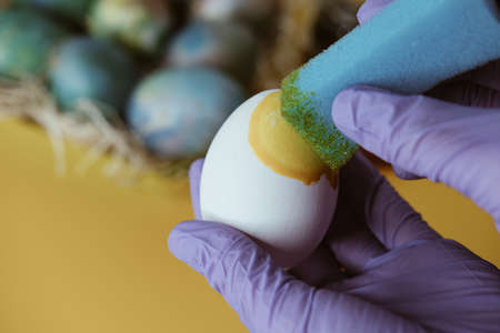 Coloring eggs for Easter. Egg in hands on a yellow background with eggs.の写真素材