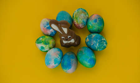 Chocolate Easter bunny lies with colorful eggs on a yellow background, close-up