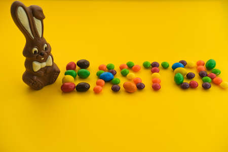 Chocolate Easter bunny lies with multi-colored sweets on a yellow background, close-up.
