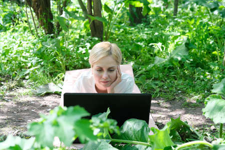 A girl works and communicates with friends on a laptop in the park. The concept is remote work via the Internet and the Covid 19 pandemicの写真素材