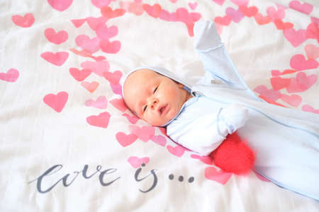 A newborn baby lies in bed on a white blanket with red hearts.の写真素材
