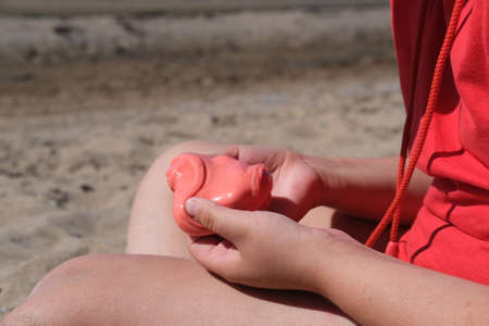 The girl has red slime in her hands. The girl is always enthusiastic about playing with slime, even on the beach playing with slime calms her down.の写真素材