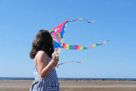 Cute little girl flying rainbow kite on sea beach.の写真素材