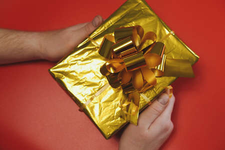 Male hands close-up on a red background.Man holds a box with a gift in his hand. Concept for Christmas, New Year 2022, Black Fridayの写真素材