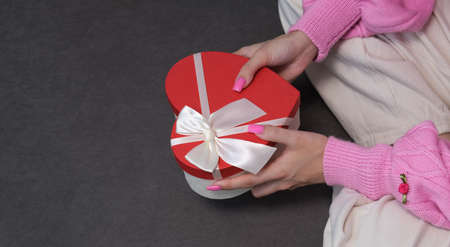 Girl holding a gift in a red box in the shape of a heart. Dark background, selective focus. Concept black friday, holiday, birthday, womens dayの写真素材