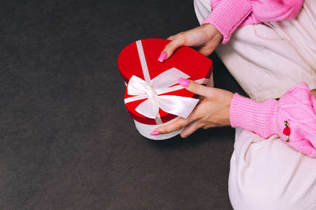 Girl holding a gift in a red box in the shape of a heart. Dark background, selective focus. Concept black friday, holiday, birthday, womens dayの写真素材